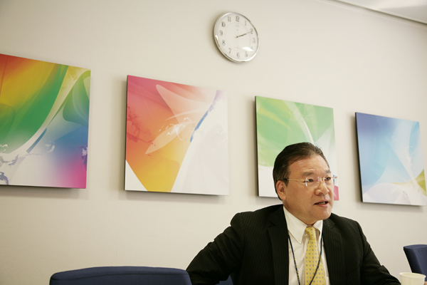 今回お話を聞かせてくださった広報部長の平尾正裕さん。背後にのぞくのは、パッケージのイメージのアートワーク。社内のミーティングルームにて