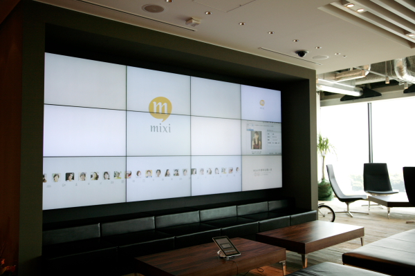 エントランスに設けられた大型スクリーン。mixiのCMなどを映し出す。手前のデスクに用意されたiPadで、映し出すものは選択できる