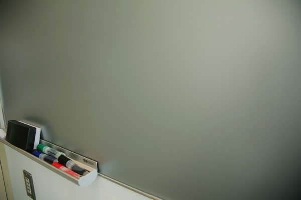 ミーティングルーム内。据え付けられたのはホワイトボードならぬシルバーボード？　いやよく見ると透明ボード？