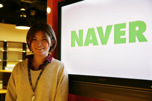 社内を案内してくださった金子智美さん。会社ロゴとともに。