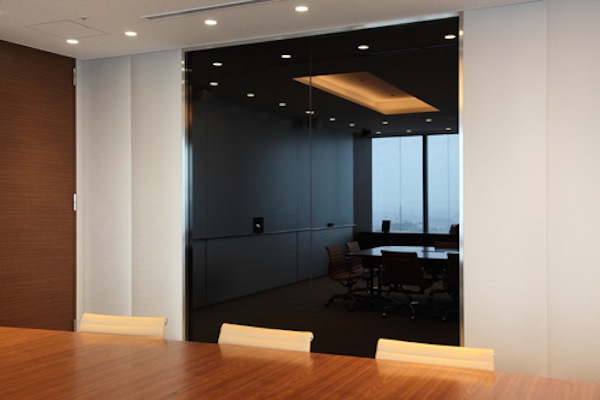 海外の人との打合せに使用するミーティングルーム。ホワイトボードを兼ねたスクリーンに相手の様子が映し出される。部屋の壁に設置されたマジックミラー越しには、通訳ブースも併設。主にエグゼクティブが使用するスペースであるせいか、インテリアはどことなくラグジュアリー