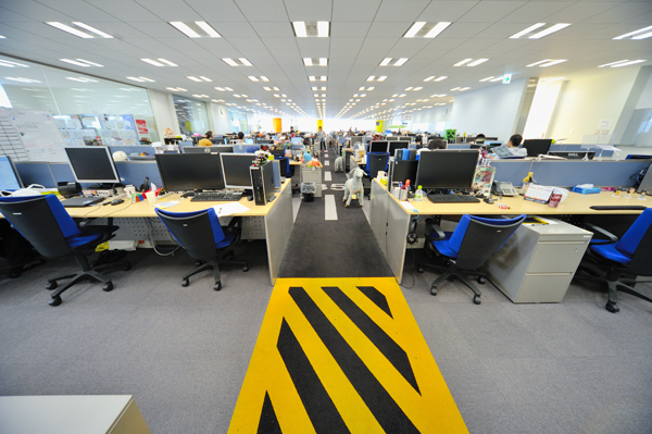 六本木ヒルズ、森タワー22階の半分を占めるワンフロアの執務室。250人の社員が席を置く。ここは主にゲームの開発に携わる人たちのフロア。所属部門（職種）毎に島を作るのではなく、プロジェクトチーム単位で、ゆるやかにまとまっている