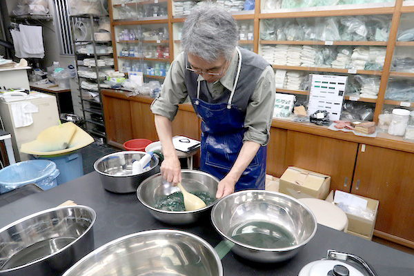 天然の「焼緑青（やきろくしょう）」の仕上げ作業をしている松下さん。 ※焼緑青……孔雀石を焼いたもの